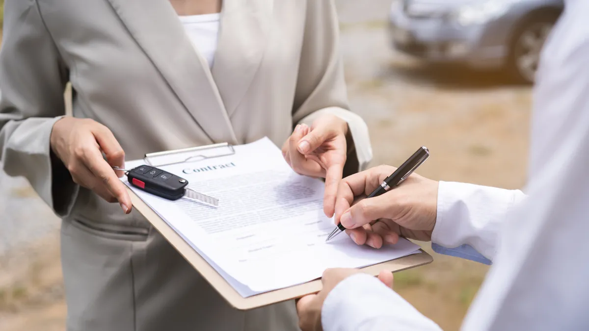 A dealer handing over car keys beside a signed vehicle transfer contract